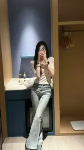 Tấm gương dài phản chiếu cô gái áo sọc quần jean đứng che mặt bằng điện thoại