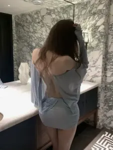 Từ phía sau cô gái váy xám trễ vai đứng cạnh giường tóc dài buông mềm