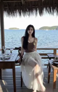 Bên hồ nước xanh, cô gái áo nâu váy be ngồi lặng, tóc thẳng rơi mềm