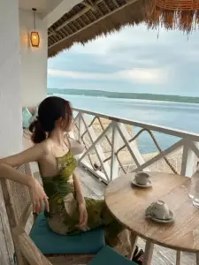 Trên ban công biển, cô nàng mặc váy xanh ngồi nghiêng, mái tóc che bớt gương mặt