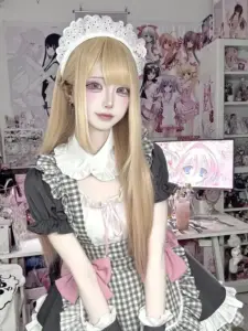 Visual tóc vàng mặc váy caro phong cách hầu gái, mỉm cười nhẹ trong căn phòng hồng dễ thương