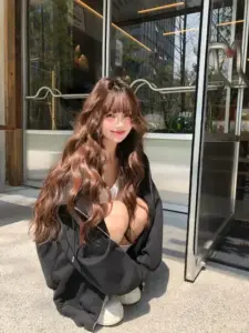 Mái tóc xoăn phủ vai, girl cute mặc đồ đen ngồi trước cửa kính và mỉm cười