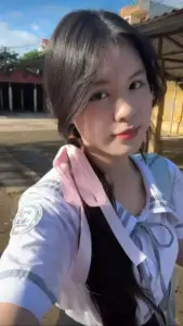 Dưới nắng ngoài trời, cô bạn chụp gần gương mặt, tóc dài buộc nơ và ánh mắt hiền