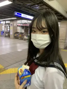 Trong nhà ga sáng đèn, cô gái đeo khẩu trang cầm chai nước, đồng phục trắng rất gọn