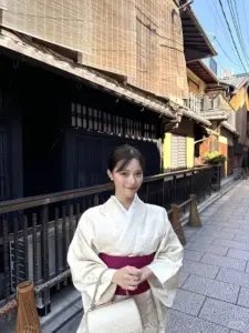 Giữa con phố cổ, cô gái mặc kimono trắng mỉm cười nhẹ, thắt obi đỏ thanh lịch
