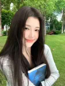 Ảnh gái xinh Trung Quốc tóc dài ôm sách xanh, đứng trong công viên với nụ cười