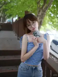 Dưới bóng cây, mỹ nhân đeo kính mặc áo caro xanh cầm máy nhỏ, nét hơi ngại