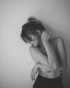 Người mẫu nữ ngồi nghiêng trong ảnh đen trắng, tóc búi cao, tay khẽ che vai trần
