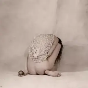 Tư thế cuộn người trên nền be nhạt làm nổi rõ vẻ đẹp cơ thể kín đáo
