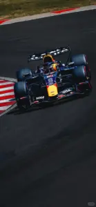 Xe Red Bull chạy một mình trên mặt cua xám, bánh trước sát dải lề đỏ trắng.