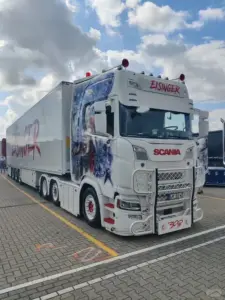 Mẫu Mercedes Actros trắng bật đèn pha trong đêm, mặt xe phản chiếu ánh sáng từ trạm xăng.