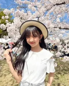 Giữa vườn hoa anh đào, cô gái đội mũ cói mỉm cười, áo trắng tạo cảm giác dịu dàng