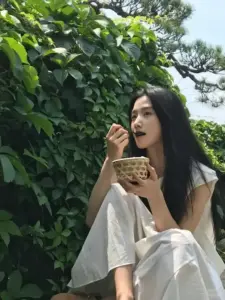 Mảng lá xanh bao quanh nàng áo đen trắng, tay cầm ly nước nhìn xa dịu nhẹ
