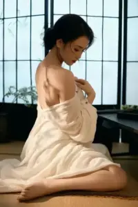Trên nền trắng sạch, cô gái ngồi ôm gối, tóc ngắn và vai trần sáng
