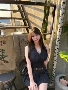 Ngồi cạnh cầu thang gỗ, nàng diện váy đen ôm dáng, tóc nâu thẳng, mắt dịu
