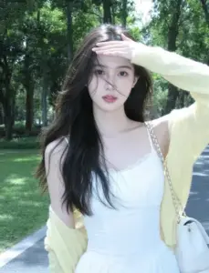 Dưới nắng công viên, cô gái váy trắng khoác cardigan vàng nhạt che tay trước tóc dài