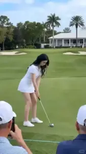 Sân golf xanh rộng hiện lên cùng cô gái mặc váy trắng cúi người chuẩn bị đánh