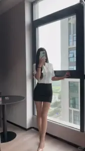 Bên cửa kính lớn cô gái áo trắng quần short đen chụp gương trong phòng sáng