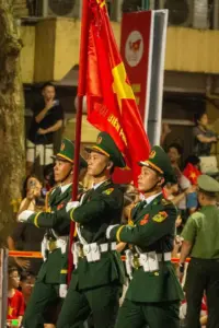 Một ba lô hành quân đặt cạnh đôi giày chiến sĩ, phía sau là người lính đang buộc lại dây áo.