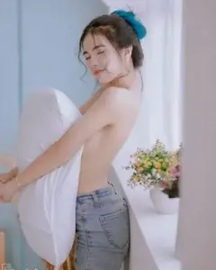 Cô gái mặc áo trắng và quần jean cười nhẹ, tay ôm bó hoa nhỏ