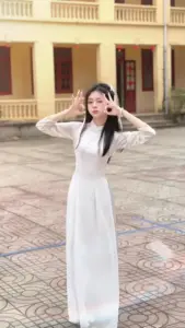 Trên sân trường vắng, cô gái mặc áo dài trắng đứng nghiêng, tay chạm tóc rất duyên