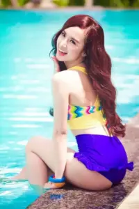 Bên làn nước xanh, Angela Phương Trinh ngồi nghiêng trong bikini sắc màu, tóc nâu rực rỡ