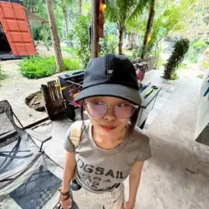Góc chụp từ trên cao bắt trọn mũ bucket đen, kính trong và nụ cười tinh nghịch