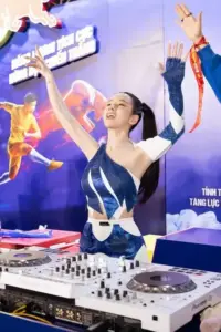Ánh đèn biểu diễn phủ quanh nữ DJ sân khấu giơ tay phấn khích bên bàn nhạc