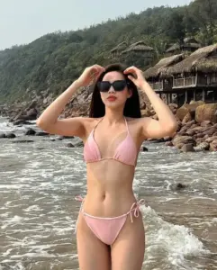 Trên bãi đá ven biển, nàng hậu đeo kính đen mặc bikini hồng tay vuốt tóc