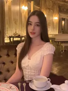 Không gian nhà hàng vàng ấm ôm lấy cô gái mặc váy hồng ren, ngồi bên tách trà