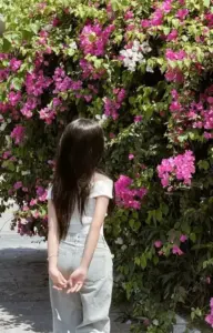 Bên giàn hoa giấy rực, cô gái chắp tay sau lưng với áo trắng giản dị