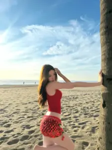 Bộ đồ bơi đỏ tôn làn da nàng đứng bên thân dừa trên bãi biển chiều