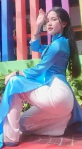 Người đẹp áo dài xanh ngồi tạo dáng bên ánh đèn đỏ, tóc uốn nhẹ và nụ cười duyên