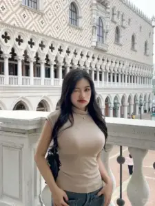 Giữa nền kiến trúc trắng, cô gái áo be đứng nhẹ nhàng với ngực căng đầy
