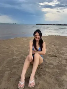 Bãi biển vắng có cô gái ngồi thư thả, bikini đen và nụ cười hơi ngại