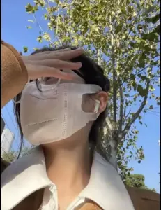 Bóng hồng đeo khẩu trang be và kính trong, đưa tay che nắng dưới tán hoa