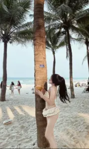 Bên hàng dừa ven biển, cô nàng mặc bikini trắng đứng nghiêng, tóc dài bay nhẹ theo gió