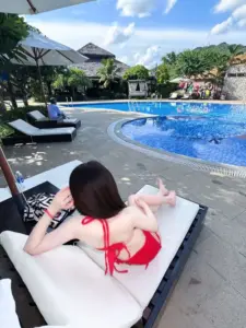 Cạnh hồ bơi xanh, dáng nằm thư giãn trên ghế trắng, bikini đỏ nổi bật sau mái tóc
