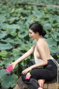 Bên hồ sen xanh mát, cô gái mặc áo be quần đen nhẹ nhàng cầm bông sen hồng