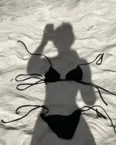 Trên cát trắng, chiếc bikini màu đen nằm cạnh bóng dáng cô gái, dây buộc trải dài