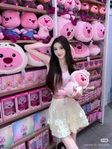 Cạnh kệ gấu bông hồng, mái tóc đen dài ôm gấu nhỏ và cười ngại ngùng