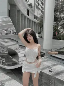 Khung hình ngoài sảnh ghi lại cô gái váy trắng, một tay vuốt tóc, dáng đứng mềm