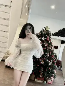 Trước gương phòng sáng, nàng mặc đầm trắng ngắn, tóc đen xõa cạnh cây thông nhỏ