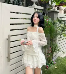 Ảnh gái xinh mặc váy ngắn sexy đứng cạnh cổng trắng, tóc đen và nụ cười hiền