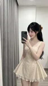 Cảnh selfie rèm xám thấy cô gái váy kem xòe, tóc buộc thấp và dáng nhỏ nhắn
