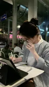 Cô nàng văn phòng mặc sơ mi trắng ngồi bên laptop với nụ cười nhẹ rất cuốn