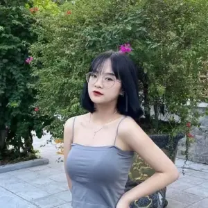 Cô gái tóc đen đeo kính tạo dáng bên hàng cây với áo hai dây xanh xám nhẹ nhàng