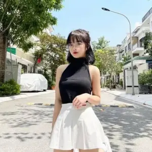 Thiếu nữ mặc áo cổ lọ đen phối chân váy trắng đứng dưới nắng với dáng vẻ tự tin