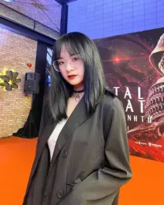 Cô gái mặc blazer tối màu đứng tại sự kiện ánh cam với mái tóc dài và ánh nhìn trầm