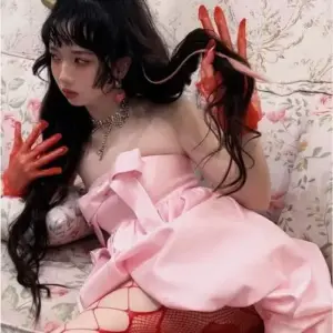 Trên nền chăn hồng, cô gái mặc váy trễ vai, tóc xoăn đen điểm nơ đỏ